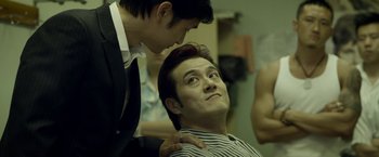 Movie still from “Revenge of the Green Dragons” (2014), directed by Andrew Loo – A man getting his hair cut by another man; Medium shot, Over the shoulder angle
