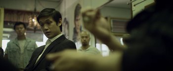 Movie still from “Revenge of the Green Dragons” (2014), directed by Andrew Loo – Two men in suits are looking at each other in a room; Medium shot, Over the shoulder angle