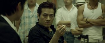 Movie still from “Revenge of the Green Dragons” (2014), directed by Andrew Loo – A man in a black shirt is holding a cigarette; Close Up shot, Low angle