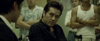 Movie still from “Revenge of the Green Dragons” (2014), directed by Andrew Loo – A person sitting in front of a group of people; Close Up shot, Over the shoulder angle