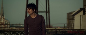 Movie still from “Revenge of the Green Dragons” (2014), directed by Andrew Loo – A young man standing in front of an iron bridge; Medium shot, Over the shoulder angle