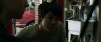 Movie still from “Revenge of the Green Dragons” (2014), directed by Andrew Loo – A young man sitting in front of a brick wall; Close Up shot, Over the shoulder angle