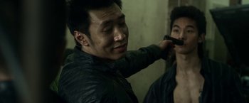 Movie still from “Revenge of the Green Dragons” (2014), directed by Andrew Loo – A man holding a gun in a room; Close Up shot, Over the shoulder angle