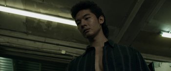 Movie still from “Revenge of the Green Dragons” (2014), directed by Andrew Loo – A young man with a black shirt is looking at the camera; Close Up shot, Low angle