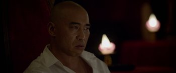 Movie still from “Revenge of the Green Dragons” (2014), directed by Andrew Loo – A man with a bald head is looking into the distance; Close Up shot, Over the shoulder angle