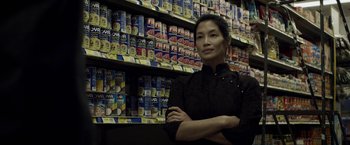 Movie still from “Revenge of the Green Dragons” (2014), directed by Andrew Loo – A woman standing in front of a wall full of food; Medium shot, Low angle