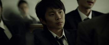 Movie still from “Revenge of the Green Dragons” (2014), directed by Andrew Loo – A man in a suit and tie sitting in a room; Close Up shot, Over the shoulder angle
