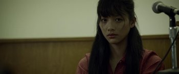 Movie still from “Revenge of the Green Dragons” (2014), directed by Andrew Loo – A woman with long black hair sitting in front of a wall; Close Up shot, Over the shoulder angle