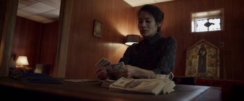 Movie still from “Revenge of the Green Dragons” (2014), directed by Andrew Loo – A woman sitting at a table holding a stack of money; Medium shot, Low angle