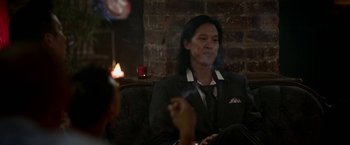 Movie still from “Revenge of the Green Dragons” (2014), directed by Andrew Loo – A man smoking a cigarette in front of a brick wall; Medium shot, Over the shoulder angle