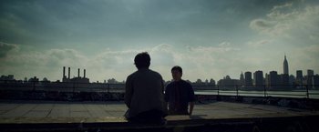 Movie still from “Revenge of the Green Dragons” (2014), directed by Andrew Loo – Two men sitting on a ledge looking out at the city; Wide shot, Over the shoulder angle
