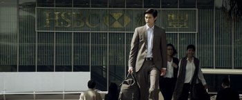 Movie still from “Revenge of the Green Dragons” (2014), directed by Andrew Loo – A man in a suit and tie walking down a street; Medium shot, Low angle