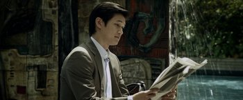 Movie still from “Revenge of the Green Dragons” (2014), directed by Andrew Loo – A man in a suit and tie reading a newspaper; Medium shot, Over the shoulder angle