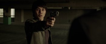 Movie still from “Revenge of the Green Dragons” (2014), directed by Andrew Loo – A man holding a gun in a room; Close Up shot, Over the shoulder angle