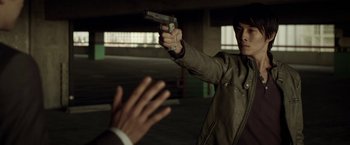 Movie still from “Revenge of the Green Dragons” (2014), directed by Andrew Loo – A man holding a gun in his hand and another man reaching out to him; Medium shot, Over the shoulder angle
