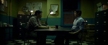 Movie still from “Revenge of the Green Dragons” (2014), directed by Andrew Loo – Two people sitting at a table in a room; Medium shot, High angle