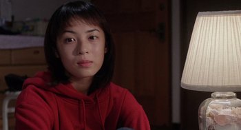 Movie still from “Ringu” (1998), directed by Hideo Nakata – A woman in a red hoodie sitting in front of a lamp; Close Up shot, High angle
