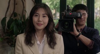 Movie still from “Ringu” (1998), directed by Hideo Nakata – A woman in a white jacket is holding a camera; Close Up shot, Over the shoulder angle