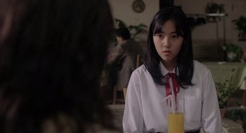 Movie still from “Ringu” (1998), directed by Hideo Nakata – A young woman sitting at a table with a glass of orange juice in front of her; Close Up shot, Over the shoulder angle