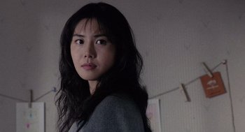 Movie still from “Ringu” (1998), directed by Hideo Nakata – A woman with long black hair is standing in a room; Close Up shot, Low angle