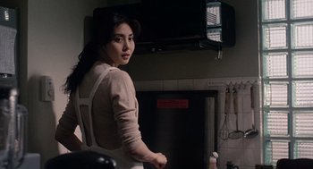 Movie still from “Ringu” (1998), directed by Hideo Nakata – A woman standing in a kitchen wearing an apron; Medium shot, Over the shoulder angle