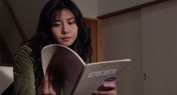 Movie still from “Ringu” (1998), directed by Hideo Nakata – A young woman reading a book in a room; Close Up shot, Low angle