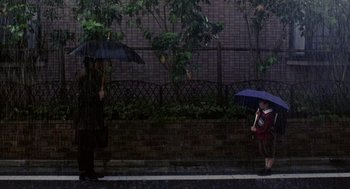 Movie still from “Ringu” (1998), directed by Hideo Nakata – A man and a woman walking down a sidewalk holding umbrellas; Extreme Wide shot, Low angle