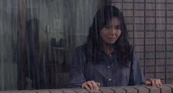 Movie still from “Ringu” (1998), directed by Hideo Nakata – A woman sitting in front of a brick wall; Medium shot, Low angle
