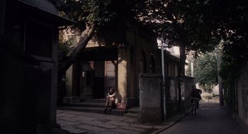 Movie still from “Ringu” (1998), directed by Hideo Nakata – A woman sitting on a bench in front of a building; Extreme Wide shot, Low angle