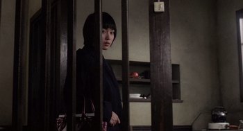 Movie still from “Ringu” (1998), directed by Hideo Nakata – A woman standing behind bars in a room; Medium shot, Low angle