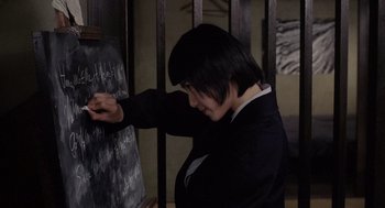 Movie still from “Ringu” (1998), directed by Hideo Nakata – A person writing on a chalkboard with chalk; Close Up shot, High angle