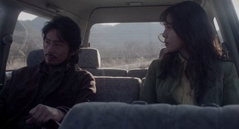 Movie still from “Ringu” (1998), directed by Hideo Nakata – A man and a woman sitting in the back of a car; Medium shot, Over the shoulder angle