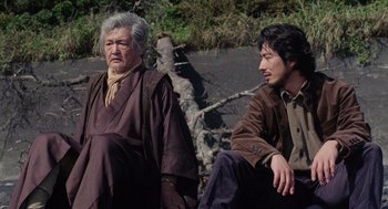 Movie still from “Ringu” (1998), directed by Hideo Nakata – Two men sitting next to each other on the ground; Medium shot, Low angle