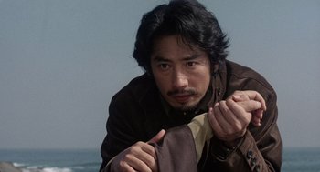 Movie still from “Ringu” (1998), directed by Hideo Nakata – A man in a brown leather jacket holding a scarf; Close Up shot, Low angle