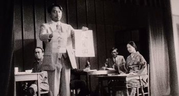 Movie still from “Ringu” (1998), directed by Hideo Nakata – An old photo of a man standing in front of a group of people; Medium shot, Low angle