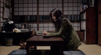 Movie still from “Ringu” (1998), directed by Hideo Nakata – A woman sitting at a table using a computer; Medium shot, High angle