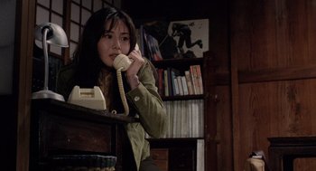 Movie still from “Ringu” (1998), directed by Hideo Nakata – A woman is talking on a phone while sitting at a desk; Medium shot, High angle