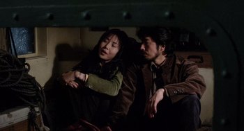 Movie still from “Ringu” (1998), directed by Hideo Nakata – A man and a woman sitting next to each other on a couch; Medium shot, High angle