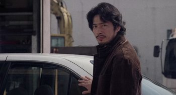 Movie still from “Ringu” (1998), directed by Hideo Nakata – A man standing in front of a white car; Close Up shot, Over the shoulder angle