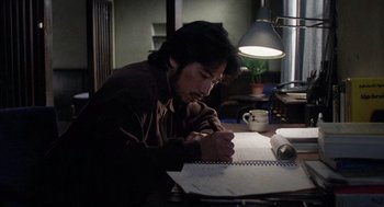 Movie still from “Ringu” (1998), directed by Hideo Nakata – A man sitting at a table writing on a piece of paper; Medium shot, High angle