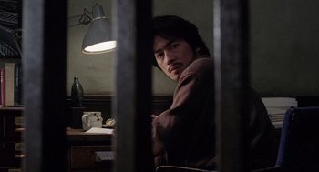 Movie still from “Ringu” (1998), directed by Hideo Nakata – A man sitting at a table in a room; Close Up shot, Low angle