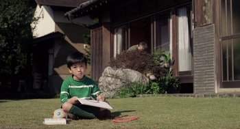 Movie still from “Ringu” (1998), directed by Hideo Nakata – A boy sitting on the grass holding a frisbee; Wide shot, High angle