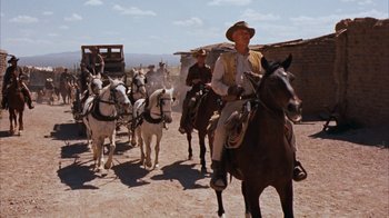 Movie still from “Rio Bravo” (1959), directed by Howard Hawks – A group of men riding horses down a dirt road; Wide shot, Low angle