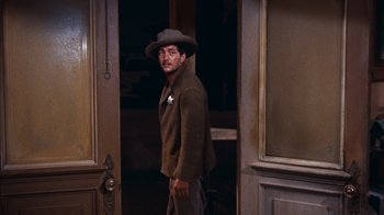 Movie still from “Rio Bravo” (1959), directed by Howard Hawks – A man standing in a doorway wearing a hat; Medium shot, Over the shoulder angle