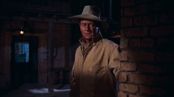 Movie still from “Rio Bravo” (1959), directed by Howard Hawks – A man wearing a hat standing next to a brick wall; Medium shot, Low angle