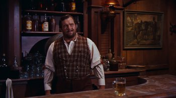 Movie still from “Rio Bravo” (1959), directed by Howard Hawks – A man standing at a bar with a glass of beer in front of him; Medium shot, Low angle