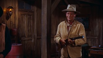 Movie still from “Rio Bravo” (1959), directed by Howard Hawks – A man holding a gun and wearing a cowboy hat; Medium shot, Over the shoulder angle