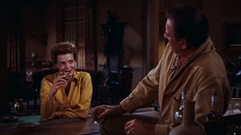Movie still from “Rio Bravo” (1959), directed by Howard Hawks – A man and a woman sitting at a table with a drink; Medium shot, Over the shoulder angle