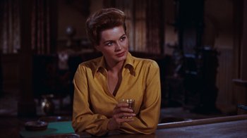 Movie still from “Rio Bravo” (1959), directed by Howard Hawks – A woman sitting at a table holding a glass; Medium shot, Low angle