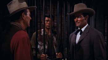 Movie still from “Rio Bravo” (1959), directed by Howard Hawks – A group of men standing next to each other in front of a brick wall; Medium shot, Over the shoulder angle